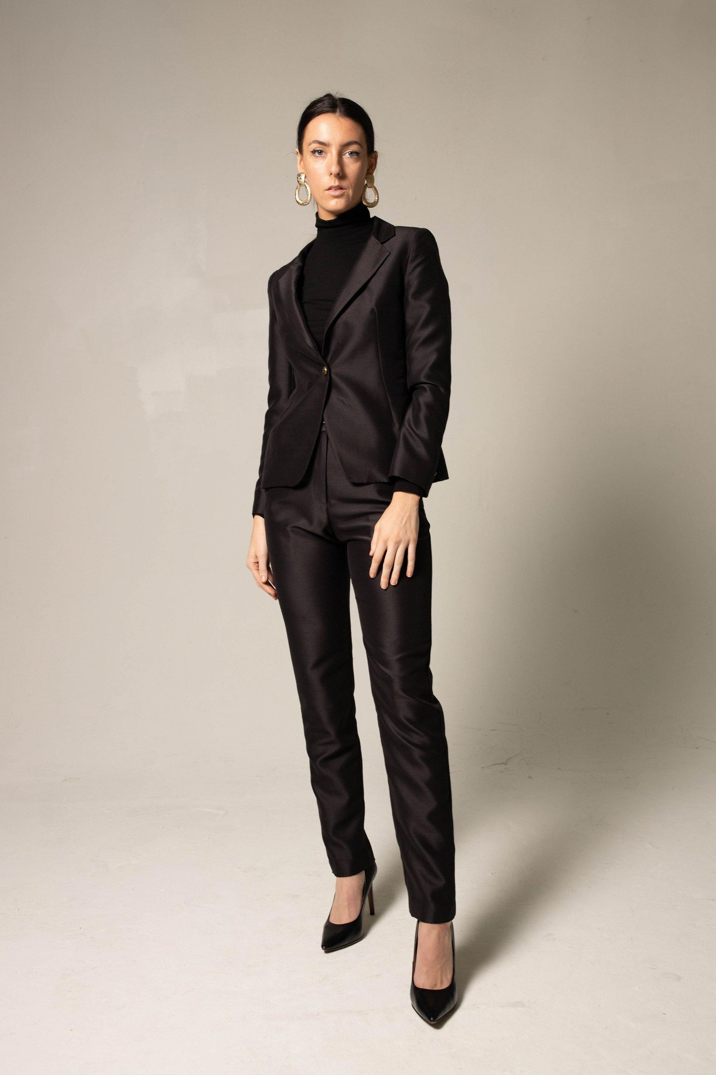 Woman wearing a sharp, tailored black suit against a plain background. This powerful lesbian outfit is a perfect example of confident lesbian fashion and sophisticated lesbian style.