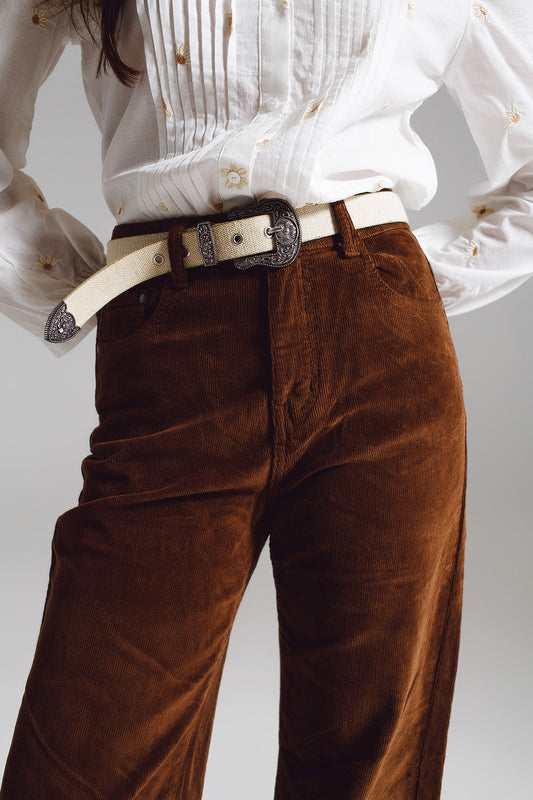 Person modeling a classic lesbian outfit of brown corduroy pants and a crisp white shirt against a light gray background. This clean look defines effortless lesbian style and is essential lesbian fashion.