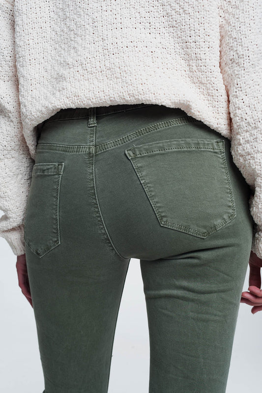 Person wearing green pants with a cozy, light-colored sweater on a plain background. This comfortable lesbian outfit is a strong example of essential lesbian clothing and confident lesbian style.