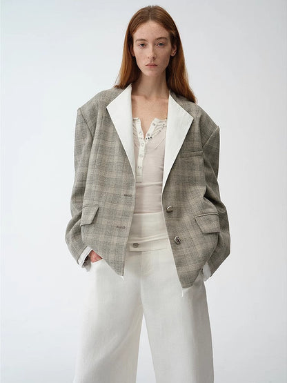 Woman wearing a gray blazer layered over a white top and light pants on a plain background. This professional lesbian outfit is a perfect example of confident lesbian fashion and modern lesbian style.