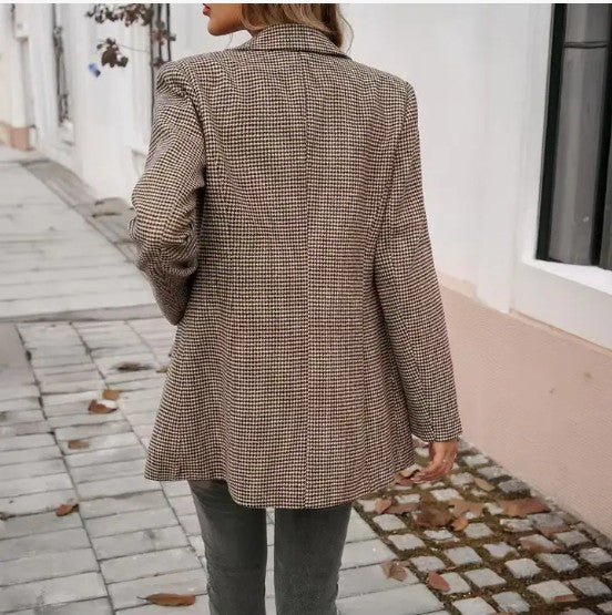 Person wearing a sharp checkered coat while walking on a sidewalk. This sophisticated lesbian outfit is a perfect example of confident lesbian fashion and classic lesbian style.
