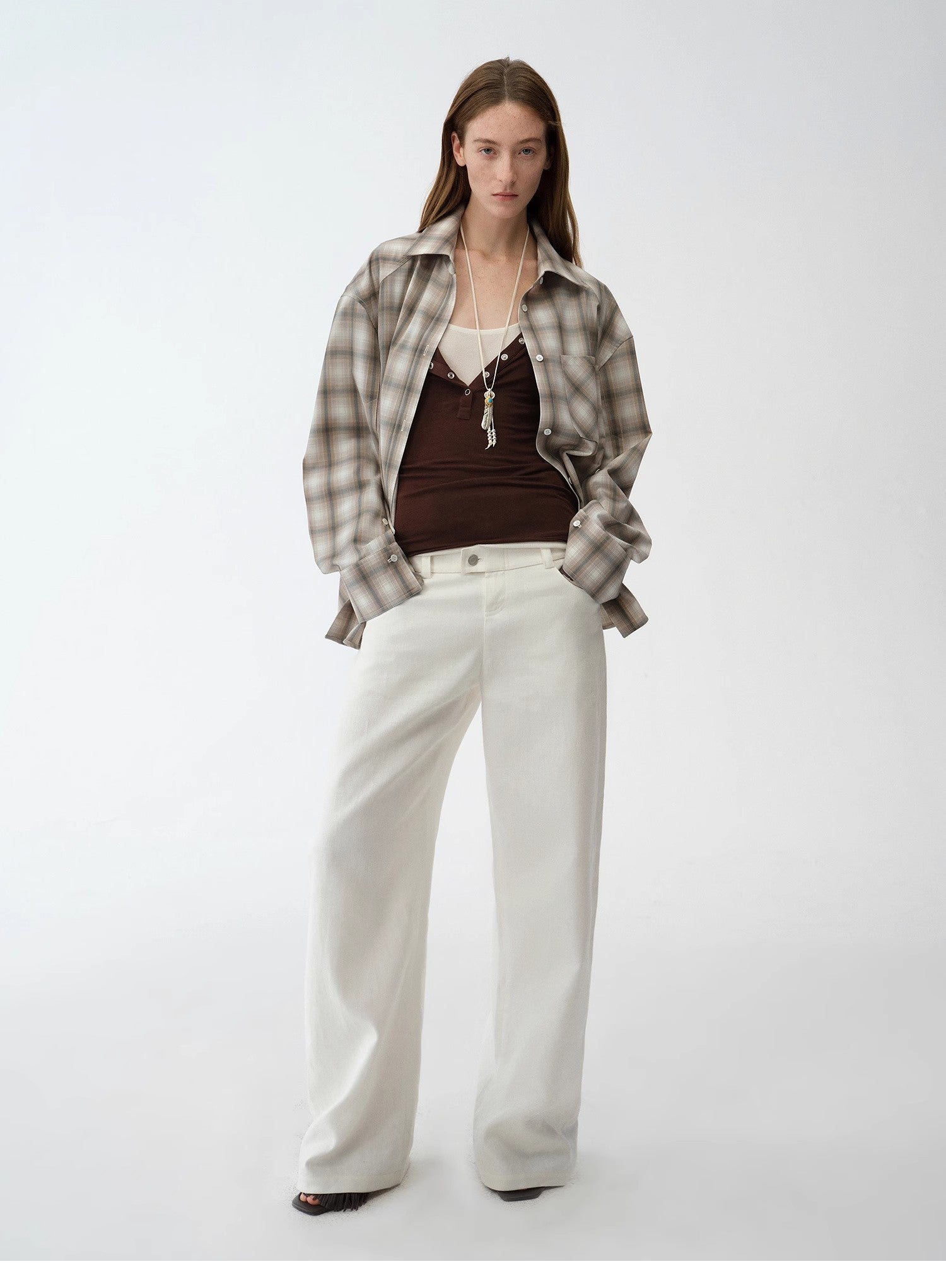 Woman wearing a plaid shirt, brown top, and white pants on a white background. This casual lesbian outfit is a perfect example of confident lesbian fashion style and effortless lesbian style.