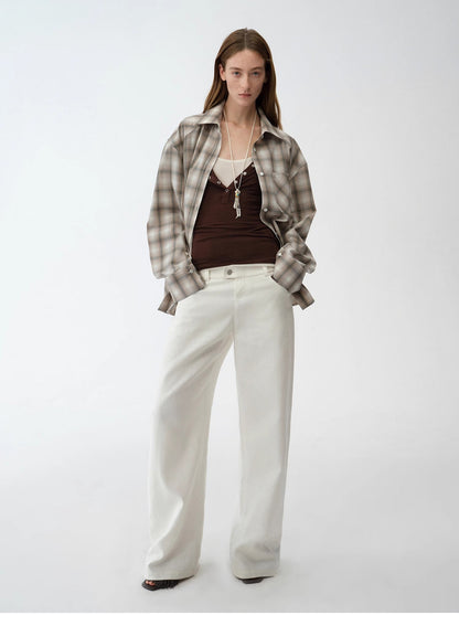 Woman wearing a plaid shirt, brown top, and white pants on a white background. This casual lesbian outfit is a perfect example of confident lesbian fashion style and effortless lesbian style.