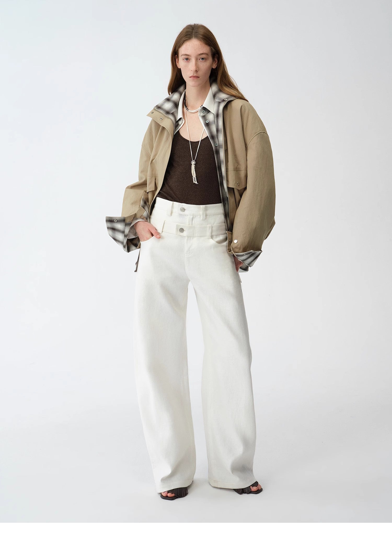 Person wearing a brown jacket, white pants, and a patterned scarf on a white background. This casual lesbian outfit is a perfect example of confident lesbian fashion style and effortless lesbian style.