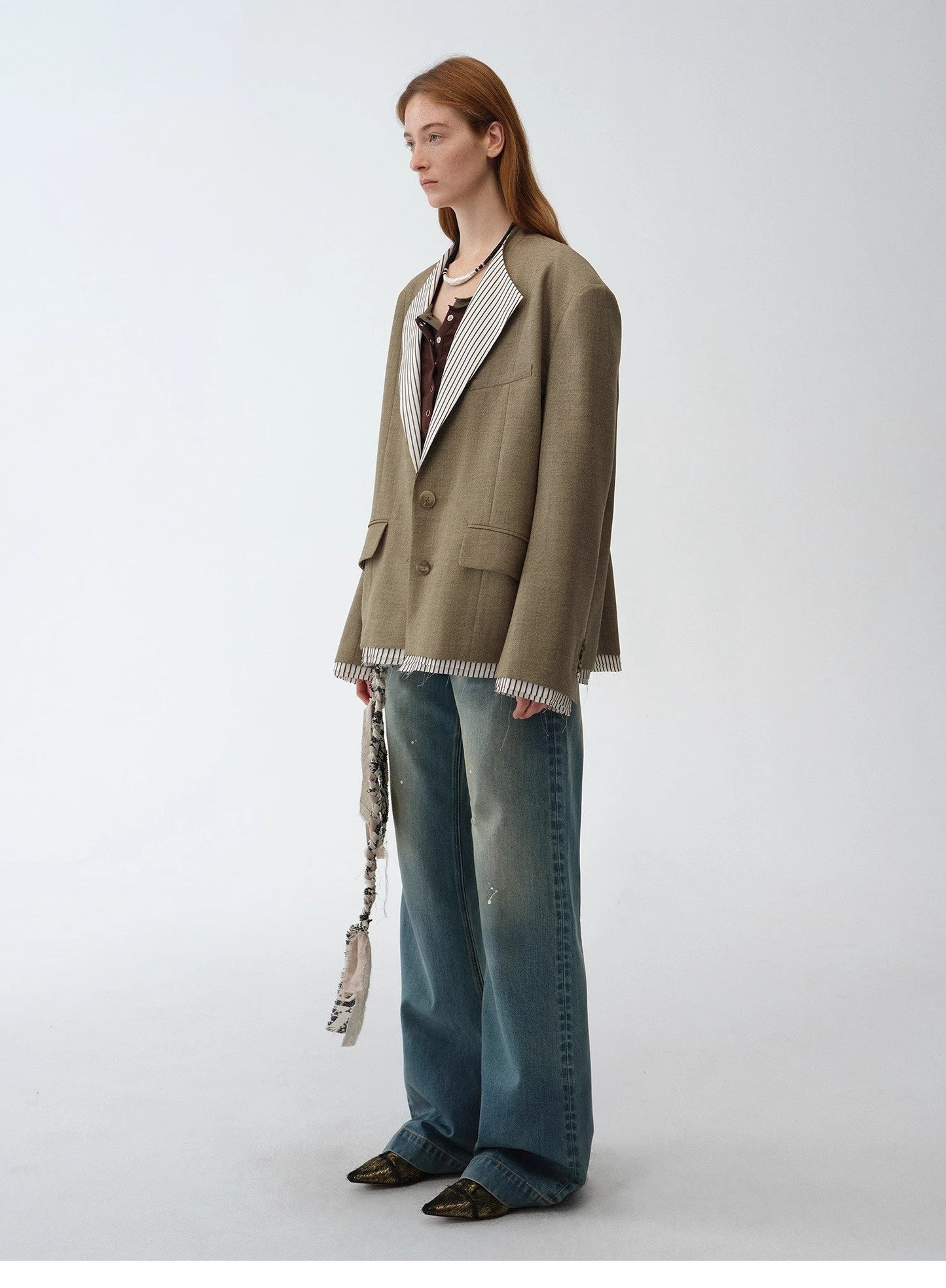 Person wearing a tailored green blazer and blue jeans on a white background. This confident lesbian outfit is a strong example of smart-casual lesbian fashion and sharp lesbian style.