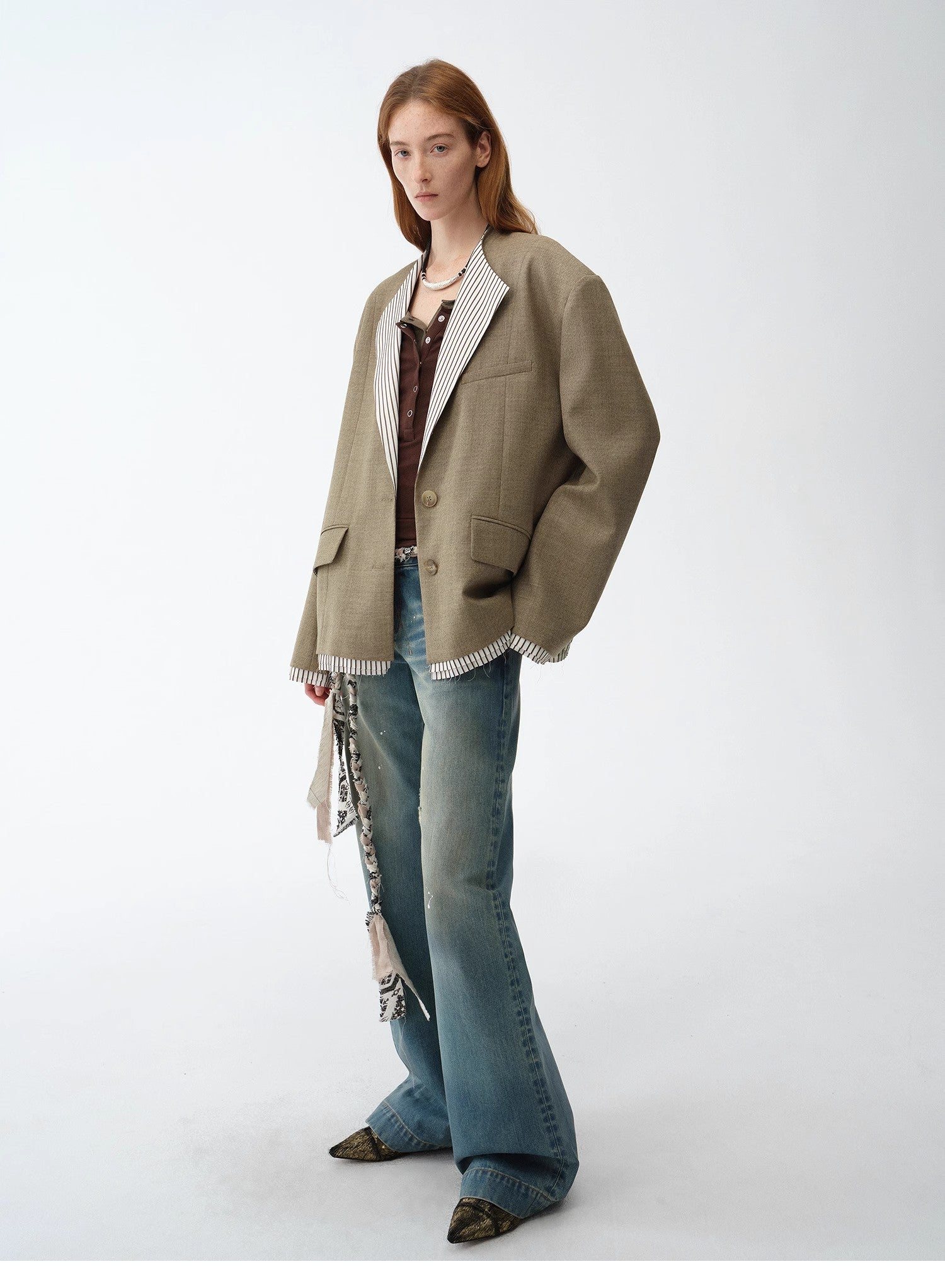Woman wearing a beige blazer layered over a patterned shirt and blue jeans on a white background. This sharp, smart-casual lesbian outfit is a perfect example of confident lesbian fashion and authentic lesbian style.