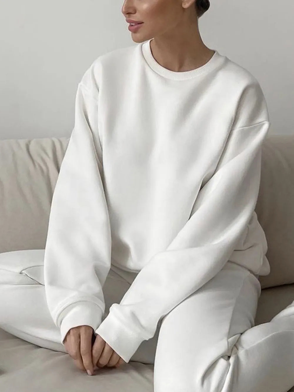 Person wearing a matching white sweatshirt and pants set, sitting comfortably on a beige couch. This comfortable lesbian outfit is a perfect example of casual lesbian clothing and relaxed lesbian style.