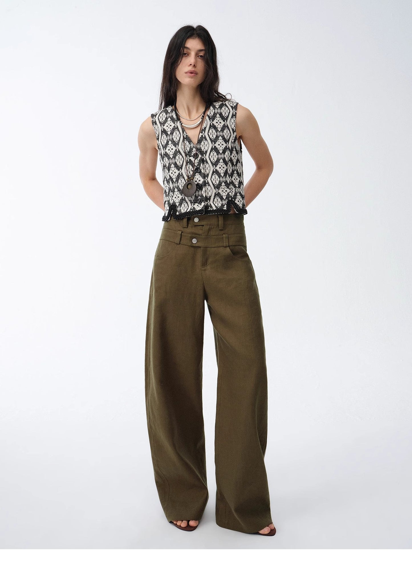 Woman wearing a sleeveless patterned top and olive green wide-leg pants on a white background. This casual lesbian outfit is a perfect example of confident lesbian fashion style and effortless lesbian style.