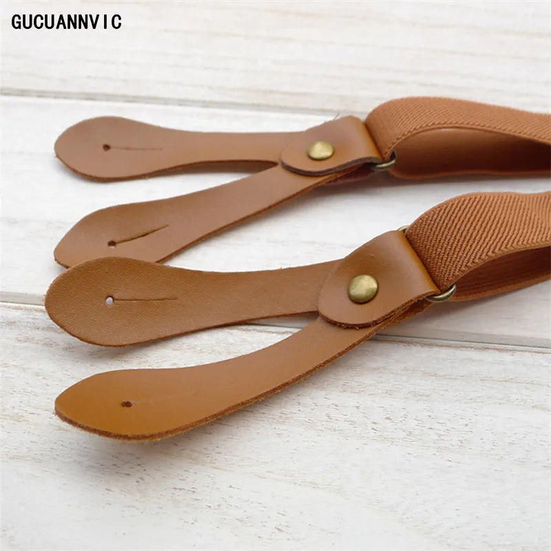 Close-up of brown leather suspenders featuring 'GUCUANNY' branding, laid on a light wooden surface. These classic accessories are essential for a sharp lesbian outfit and defining an authentic lesbian style.