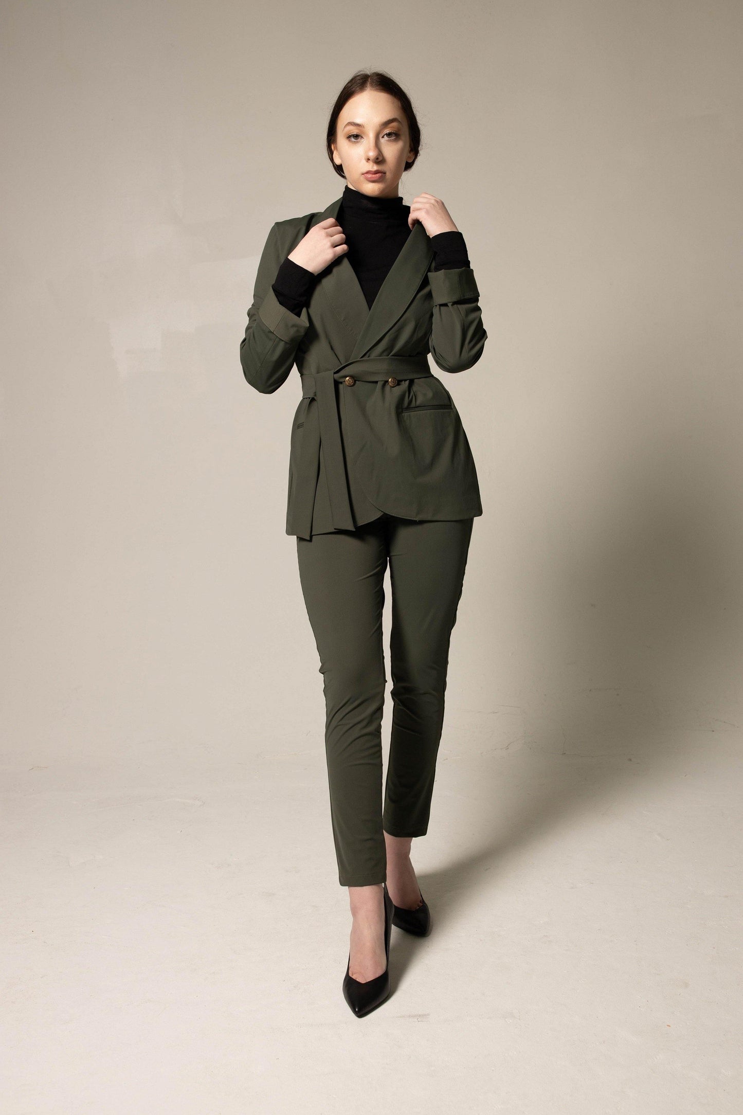 Woman wearing a tailored green suit on a plain background. This sharp, professional lesbian outfit is a perfect example of formal lesbian fashion and sophisticated lesbian style.