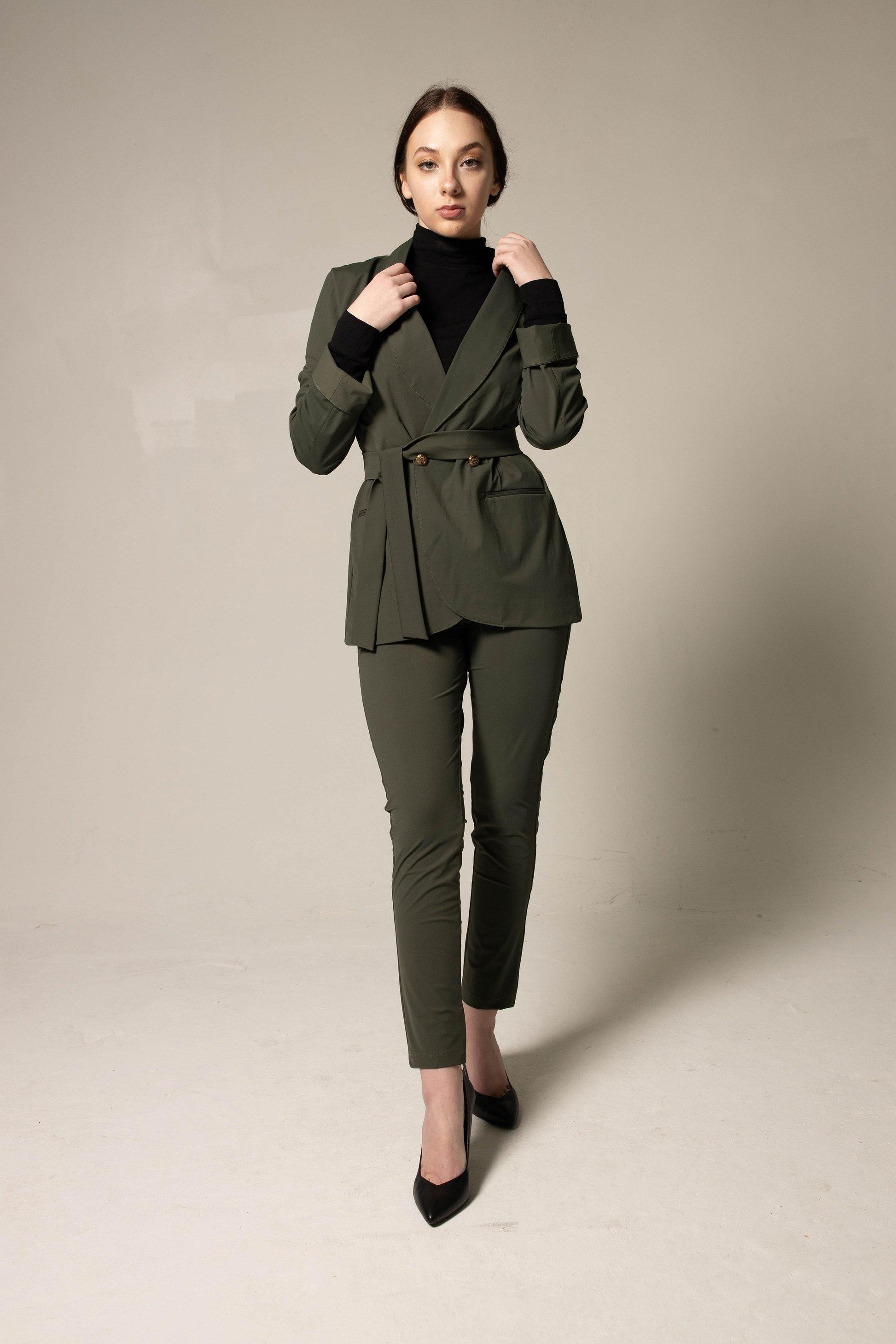 Woman wearing a tailored green suit on a plain background. This sharp, professional lesbian outfit is a perfect example of formal lesbian fashion and sophisticated lesbian style.