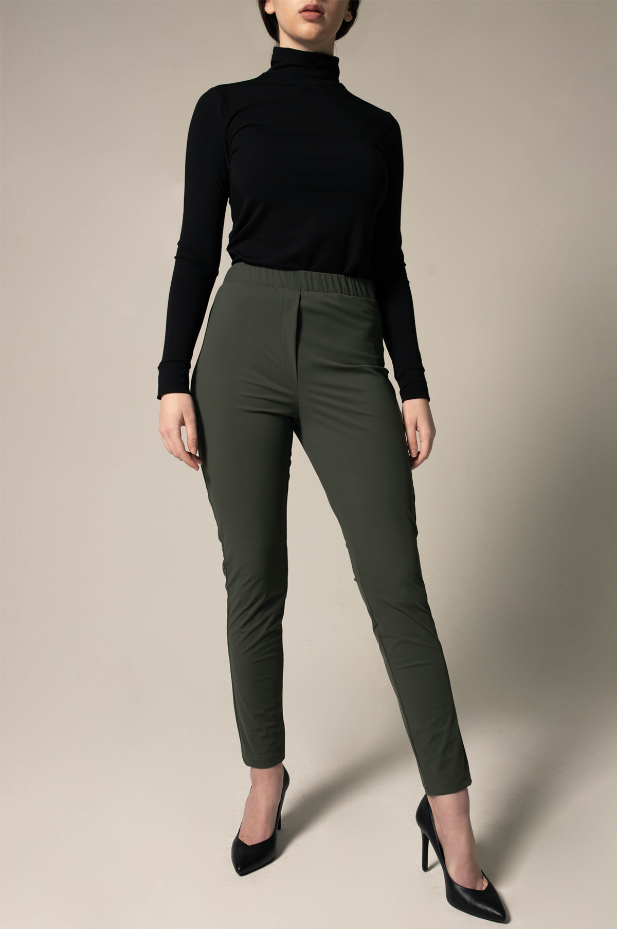 Person wearing a black turtleneck and loose green pants against a beige background. This stylish lesbian outfit is a sharp example of lesbian fashion style and confident lesbian attire.