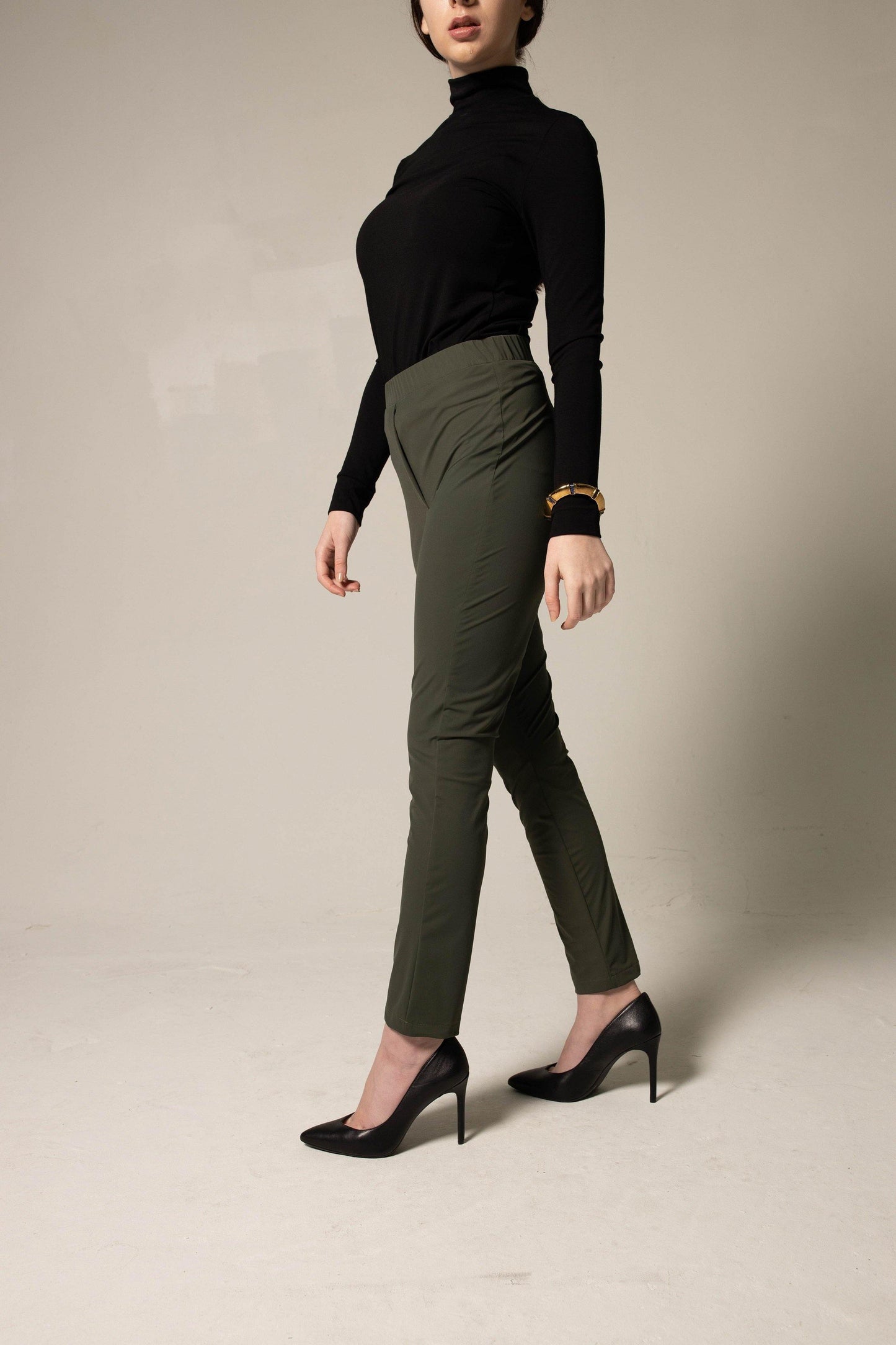 Person wearing a classic black turtleneck and wide-leg green pants on a plain background. This sharp lesbian outfit is a strong example of confident lesbian fashion style and authentic lesbian style.