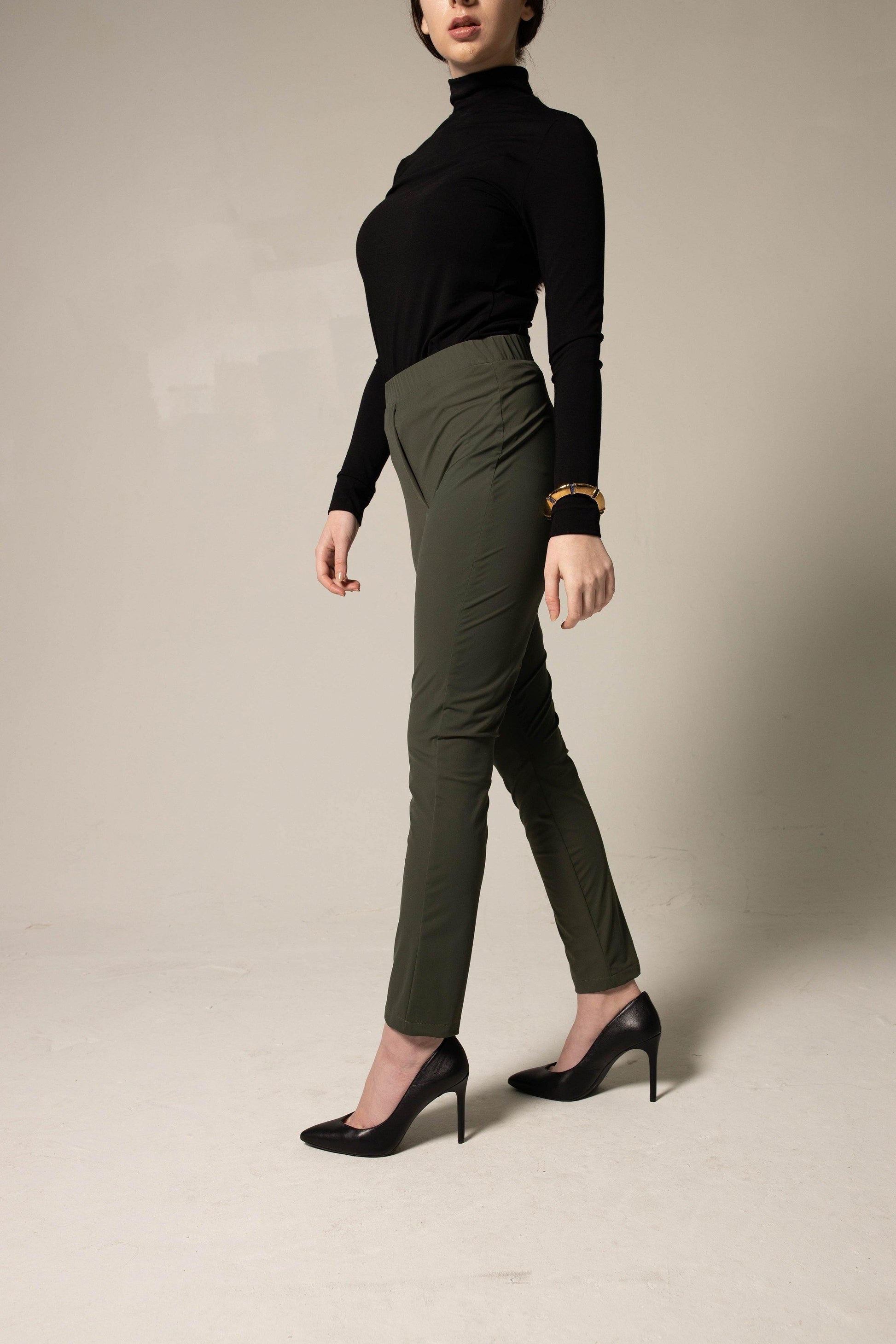 Person wearing a classic black turtleneck and wide-leg green pants on a plain background. This sharp lesbian outfit is a strong example of confident lesbian fashion style and authentic lesbian style.