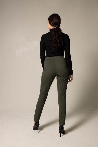 Woman modeling a simple black top and loose green pants against a beige background. This stylish lesbian outfit is a sharp example of confident lesbian fashion and authentic lesbian style.