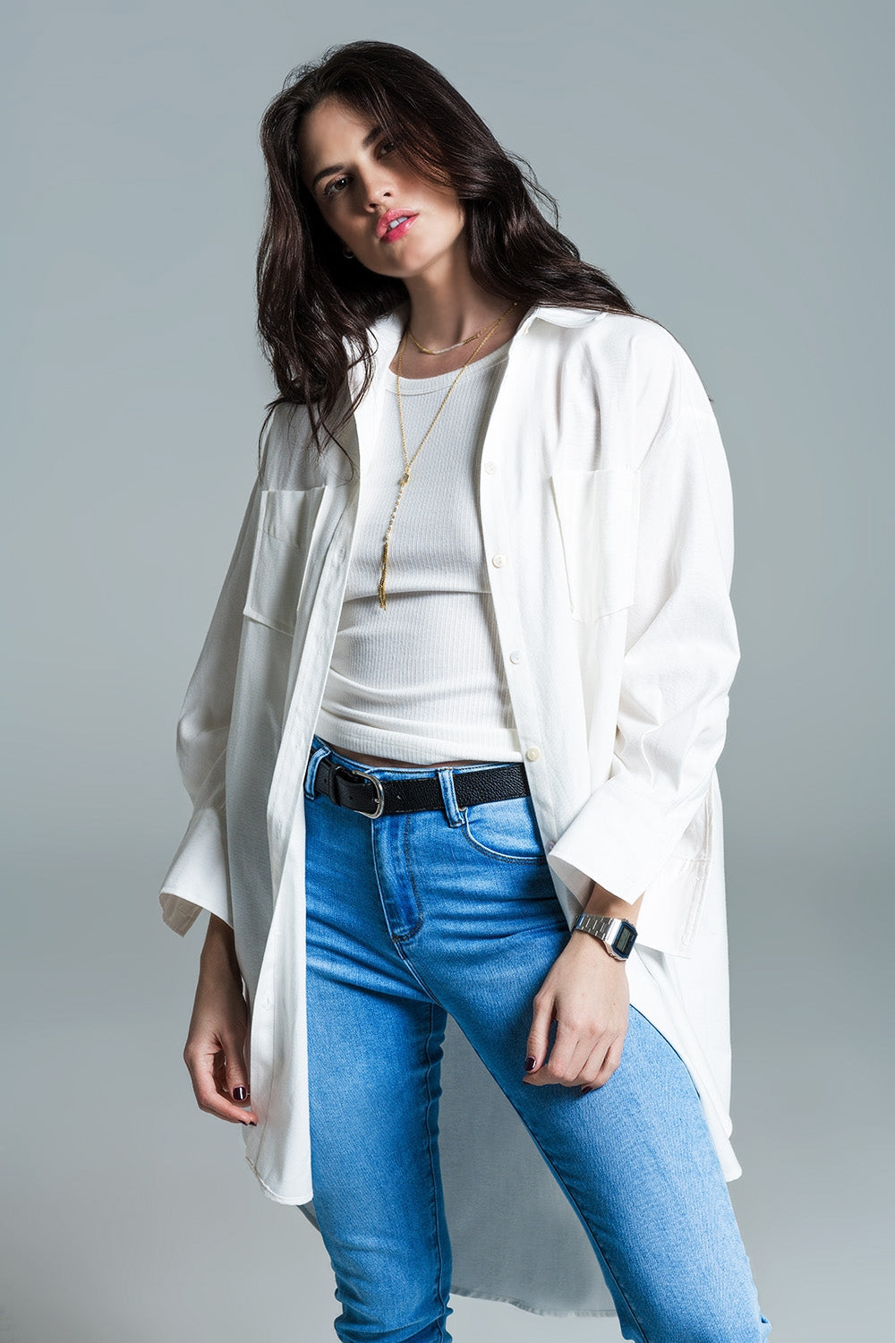 Woman wearing a white shirt, blue jeans, and a white jacket on a gray background. This classic layered lesbian outfit is a perfect example of confident lesbian fashion and authentic lesbian style.