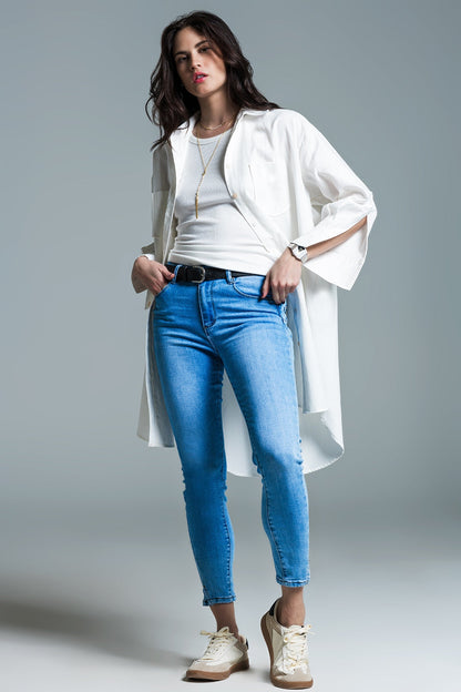 Woman wearing a white shirt, blue jeans, and a long white coat on a gray background. This sharp, layered lesbian outfit is a perfect example of confident lesbian fashion and chic lesbian style.