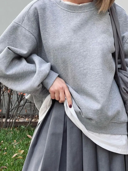 Person wearing a stylish gray sweater and matching skirt against a blurred background. This coordinated lesbian outfit is a perfect example of chic lesbian fashion and sophisticated lesbian style.