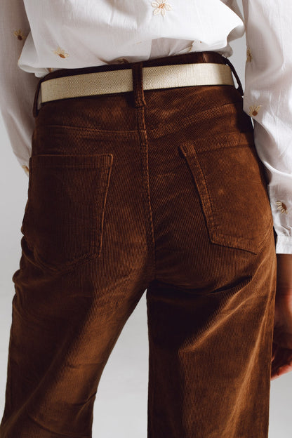 Brown corduroy pants worn with a crisp white shirt on a plain background. This classic look is an essential piece of lesbian fashion that defines confident, everyday lesbian style and a sharp lesbian outfit.