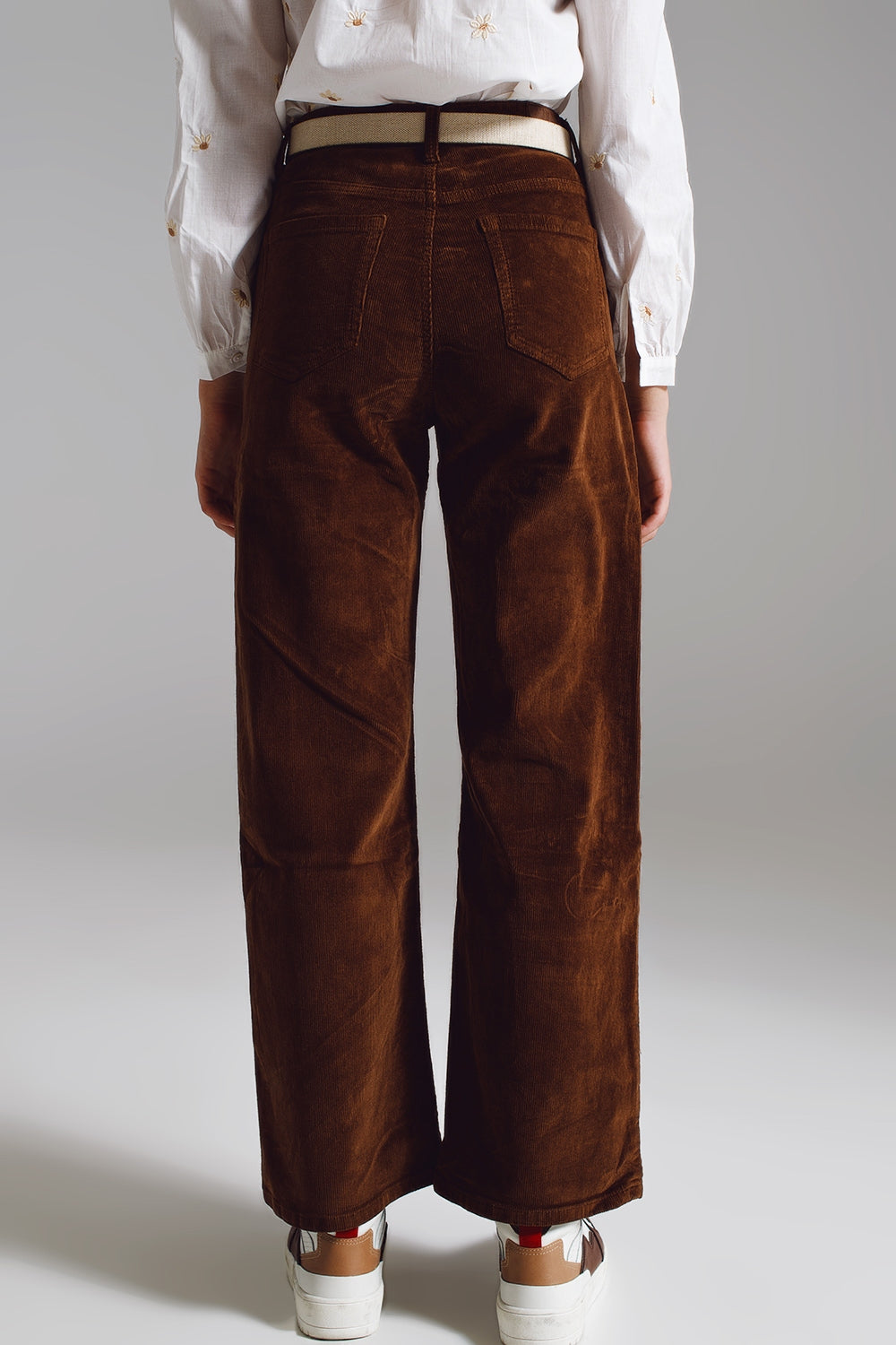 Woman modeling a simple, professional lesbian outfit featuring a white blouse and brown pants on a plain background. This look is a strong example of everyday lesbian fashion and clean lesbian style.
