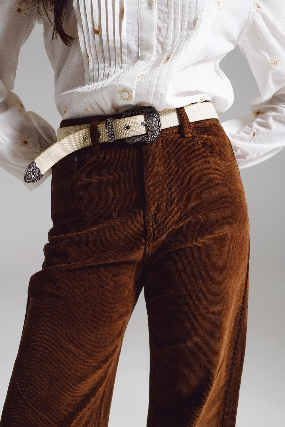 Person modeling a classic lesbian outfit of brown corduroy pants and a crisp white shirt against a light gray background. This clean look defines effortless lesbian style and is essential lesbian fashion.