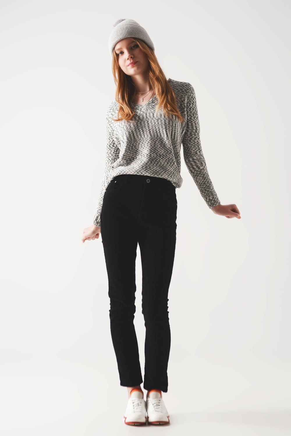 Woman wearing a cozy gray knit sweater, black pants, and white sneakers on a white background. This comfortable lesbian outfit is a perfect example of casual lesbian fashion and authentic lesbian style.