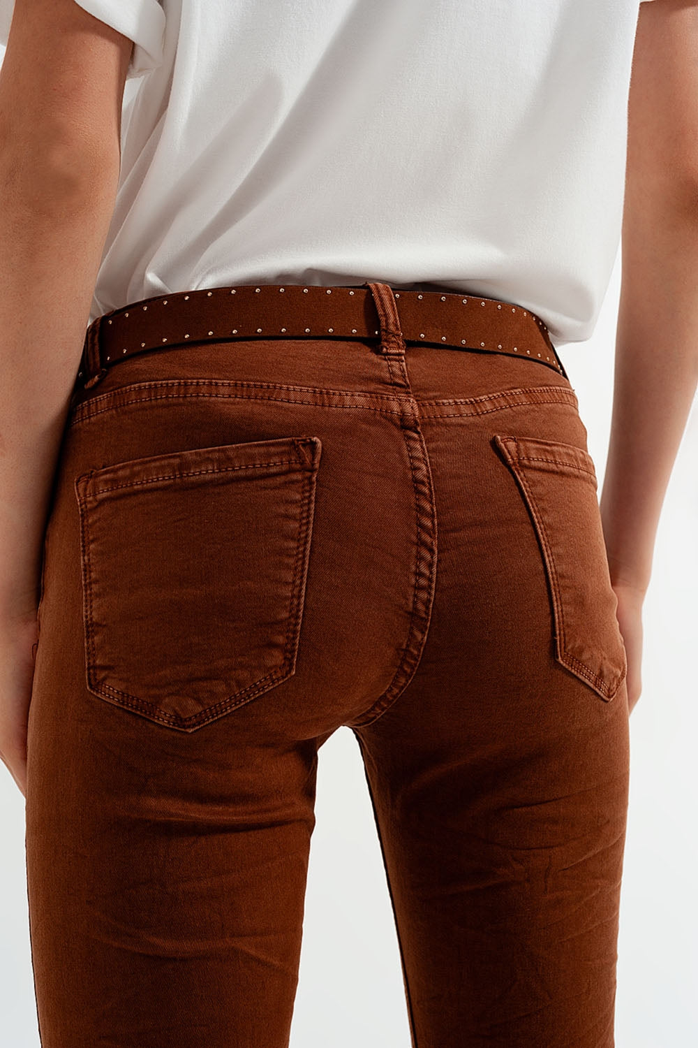Person wearing brown pants accessorized with a sharp studded belt against a plain background. This confident lesbian outfit is a perfect example of androgynous lesbian fashion and authentic lesbian style.