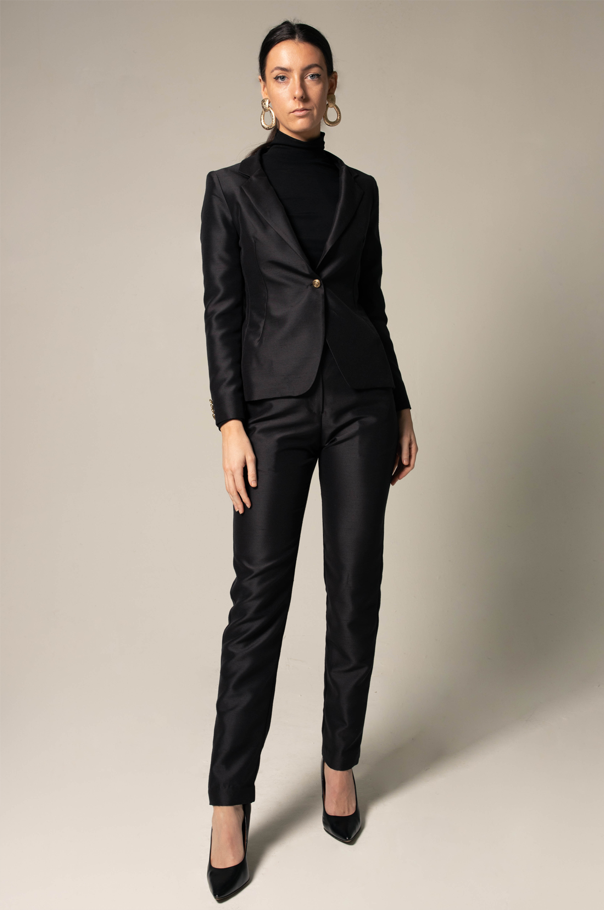 Woman wearing a sharp black suit against a neutral background. This powerful and sophisticated lesbian outfit is a perfect example of formal lesbian fashion and confident lesbian style.