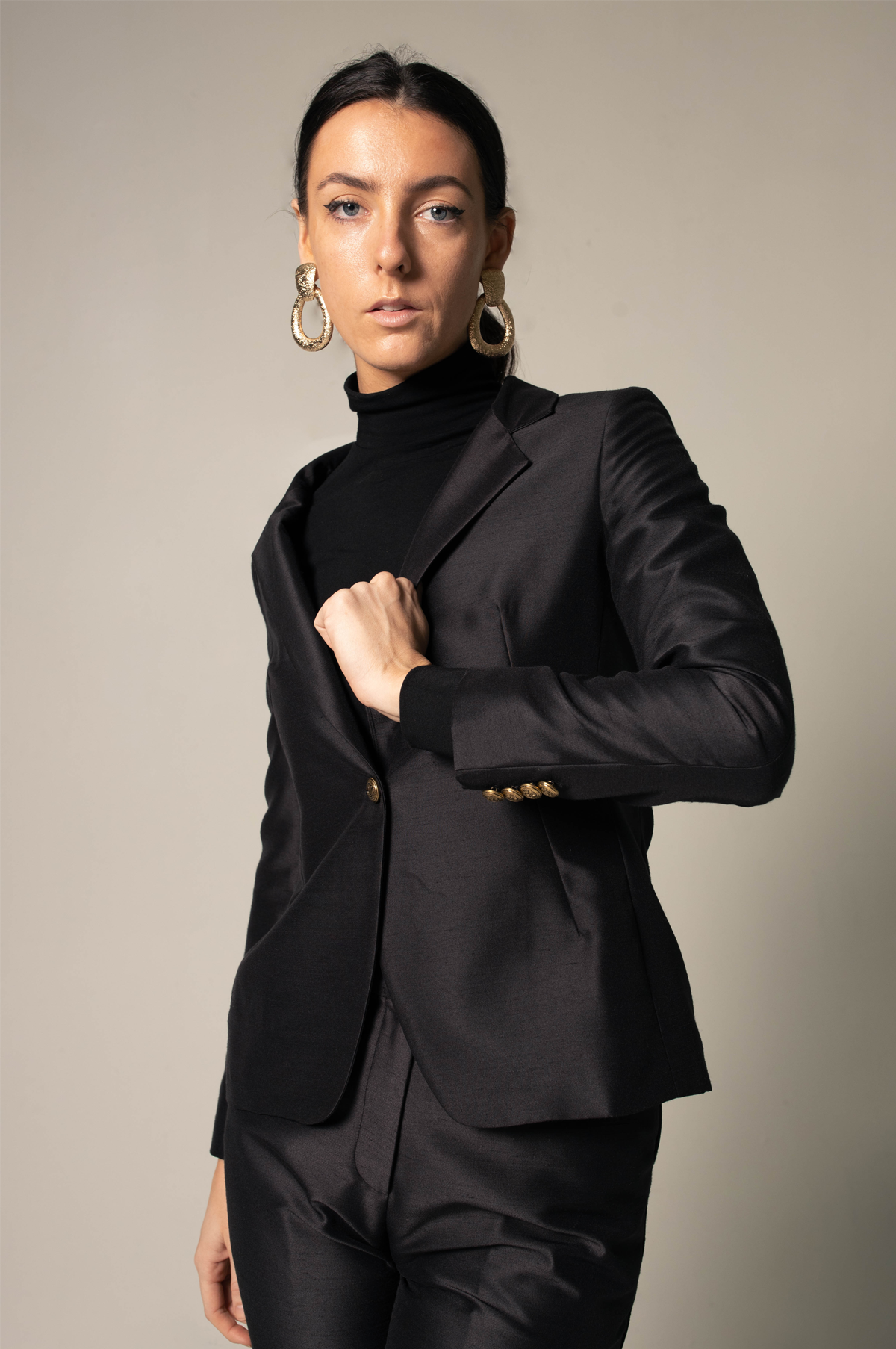 Woman wearing a sharp black suit against a neutral background. This powerful and sophisticated lesbian outfit is a perfect example of formal lesbian fashion and confident lesbian style.