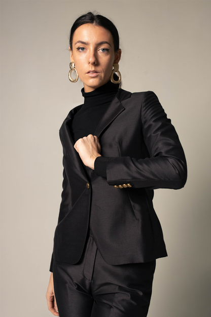 Woman wearing a sharp black suit against a neutral background. This powerful and sophisticated lesbian outfit is a perfect example of formal lesbian fashion and confident lesbian style.
