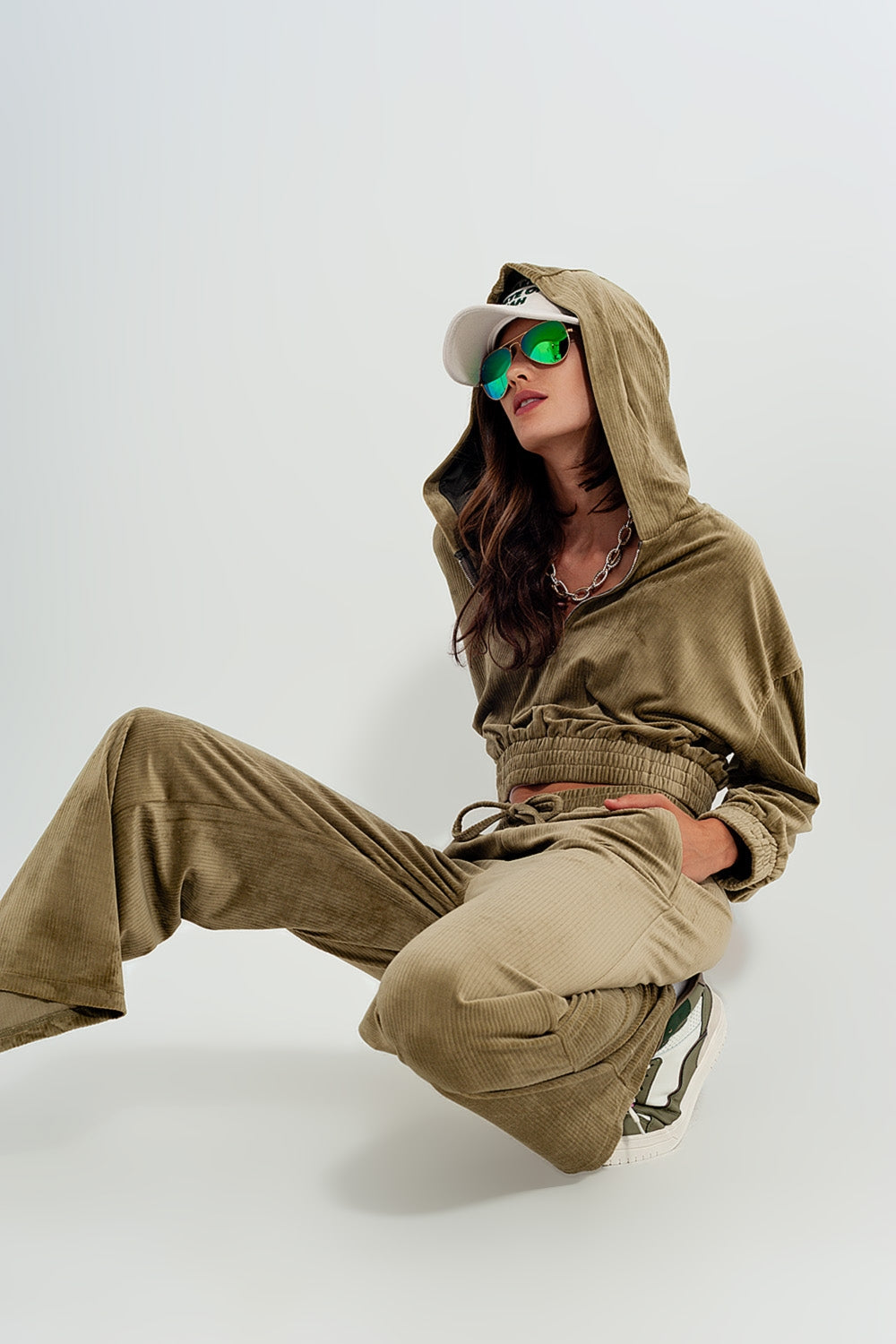 Person sitting on a white background, wearing a cozy brown hoodie and comfortable beige pants. This relaxed lesbian outfit is a perfect example of casual lesbian clothing and authentic lesbian style.