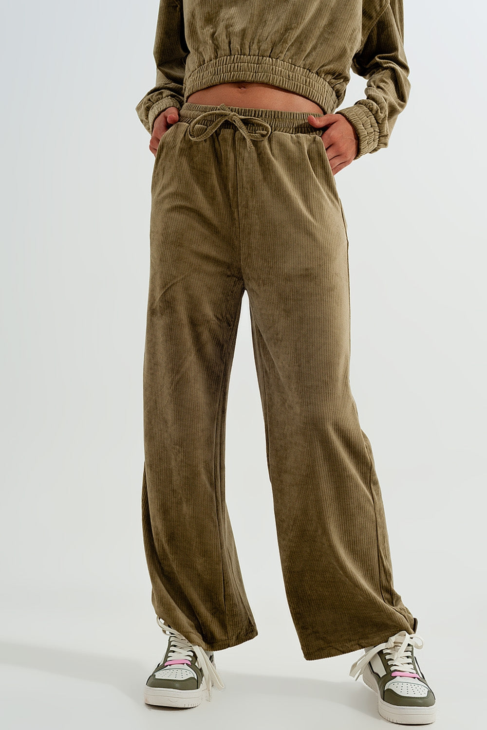 Person wearing stylish olive green corduroy pants and a matching top on a white background. This monochrome lesbian outfit is a perfect example of confident lesbian fashion and authentic lesbian style.