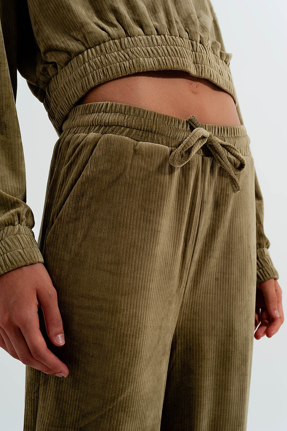 Person wearing classic olive green corduroy pants against a plain background. This confident piece is an essential component for building a sharp lesbian outfit and defining authentic lesbian style.