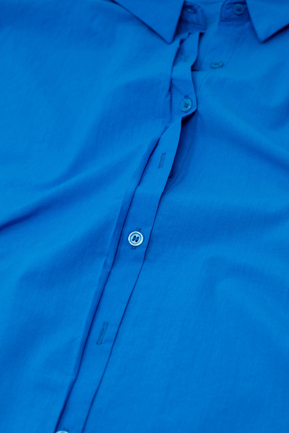 Close-up of a crisp blue shirt on a white background. This classic lesbian outfit staple is perfect for confident lesbian fashion and sharp lesbian style.