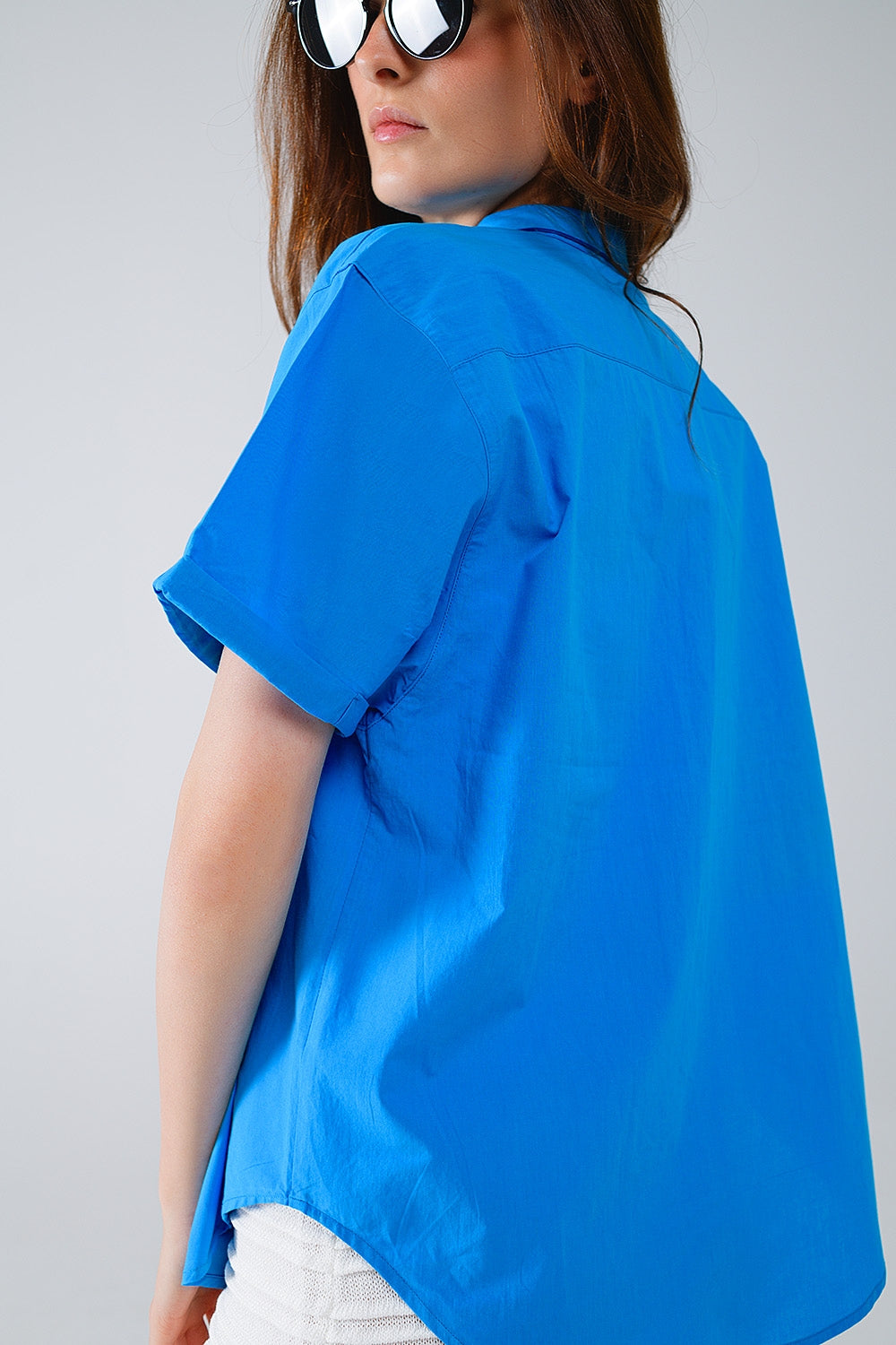 Person wearing a crisp blue shirt and confident sunglasses against a plain background. This casual lesbian outfit is a perfect example of timeless lesbian fashion and authentic lesbian style.