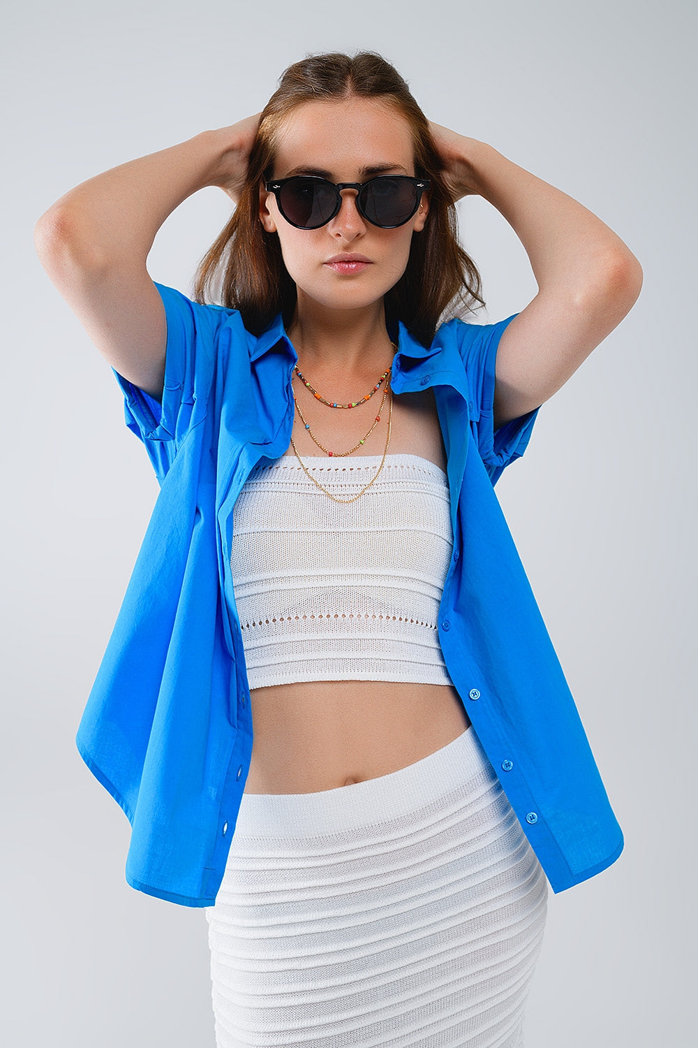 Woman wearing a blue button-up shirt layered over a crisp white top and skirt against a plain background. This casual lesbian outfit is a perfect example of confident lesbian fashion and authentic lesbian style.