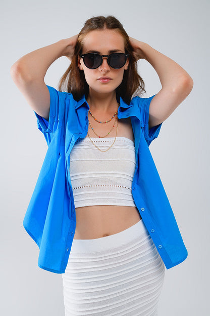 Woman wearing a blue button-up shirt layered over a crisp white top and skirt against a plain background. This casual lesbian outfit is a perfect example of confident lesbian fashion and authentic lesbian style.