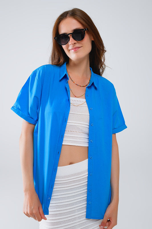 Woman wearing a blue button-up shirt layered over a crisp white top and skirt against a plain background. This casual lesbian outfit is a perfect example of confident lesbian fashion and authentic lesbian style.