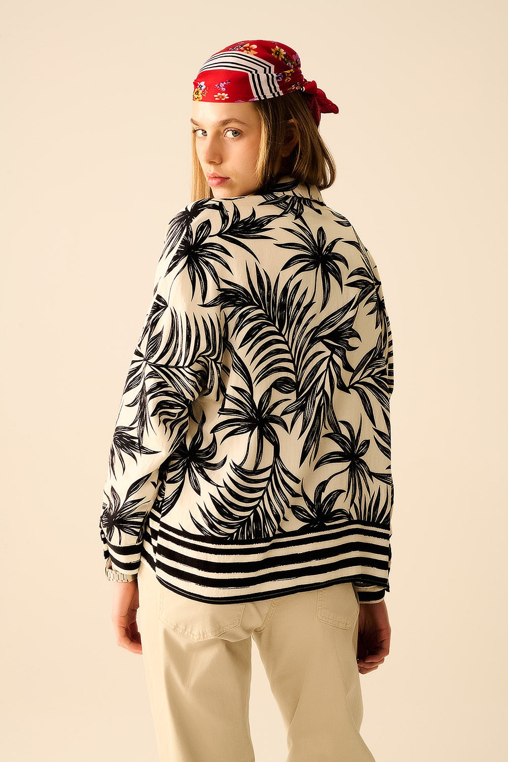 Person wearing a patterned shirt with palm leaves and a bright red headband against a beige background. This confident lesbian outfit is a perfect example of casual lesbian fashion and authentic lesbian style.