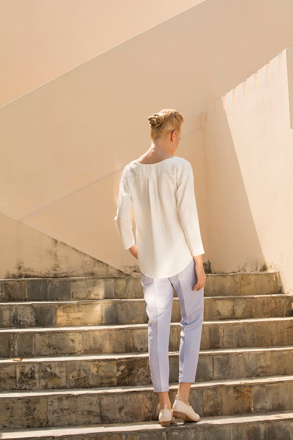 Person wearing a confident white outfit (top and bottom) while standing on stone steps with a neutral wall background. This monochrome lesbian outfit is a perfect example of clean lesbian fashion and authentic lesbian style.